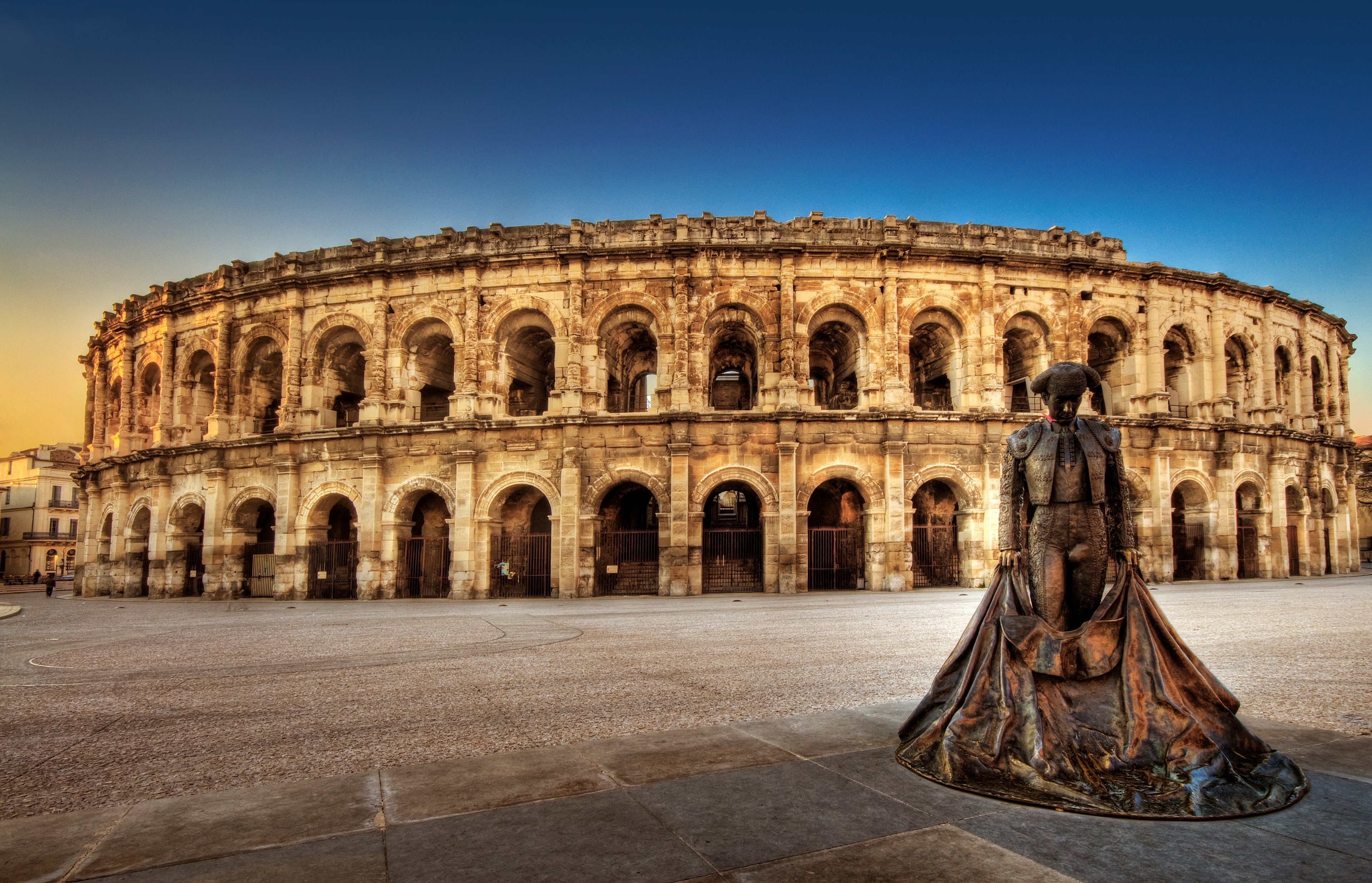arènes de nimes sous un couché de soleil avec en premier ^lan la statut d'un toréador