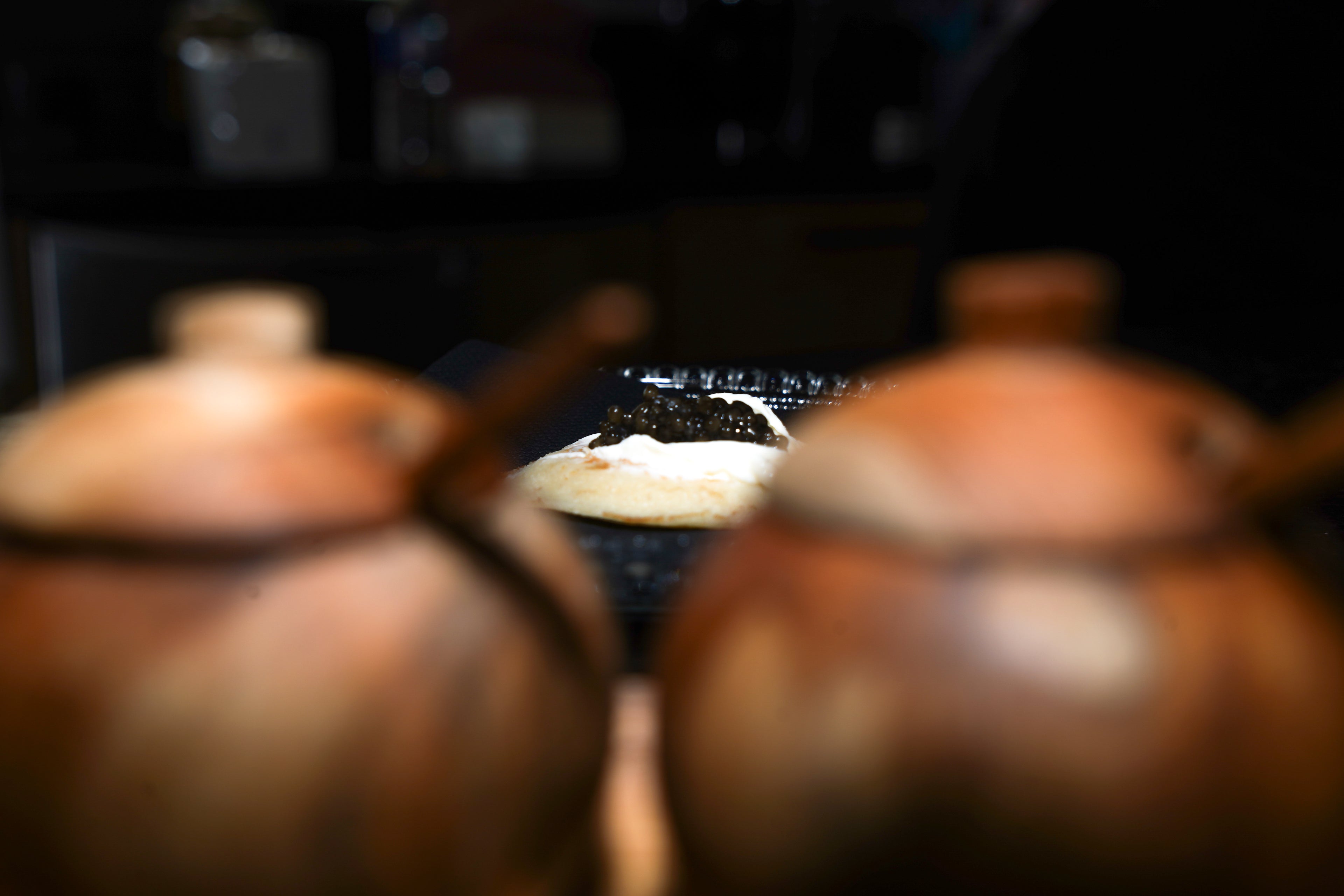 blini avec du formage frais et quelques grains de caviar baeri en arrière plan derrière deux bocaux en bois